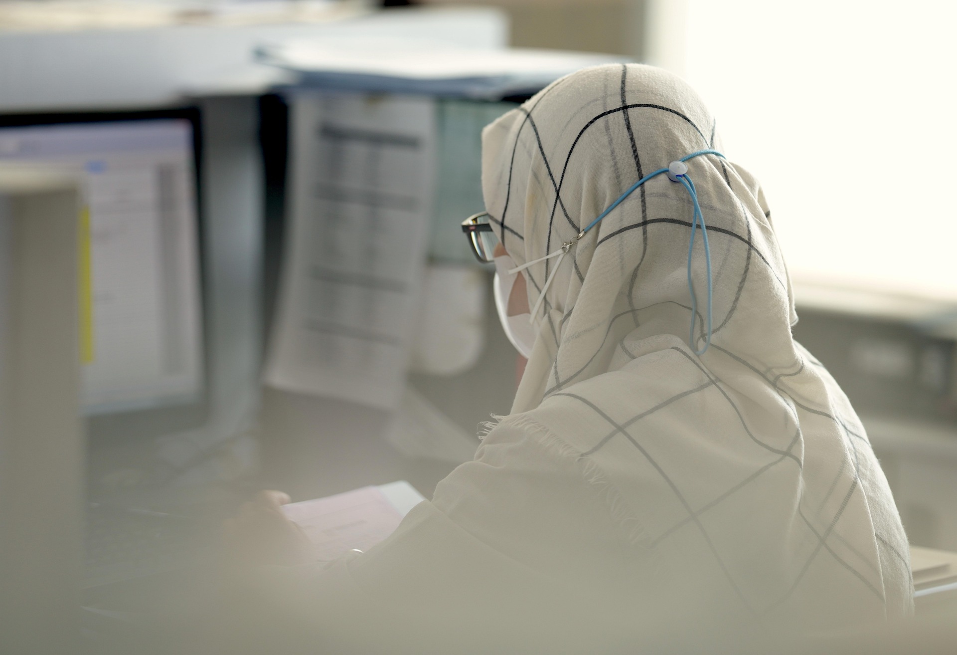 امرأة مسلمة محجبة ترتدي نظارات طبية وتعمل على شاشة كمبيوتر في بيئة مكتبية